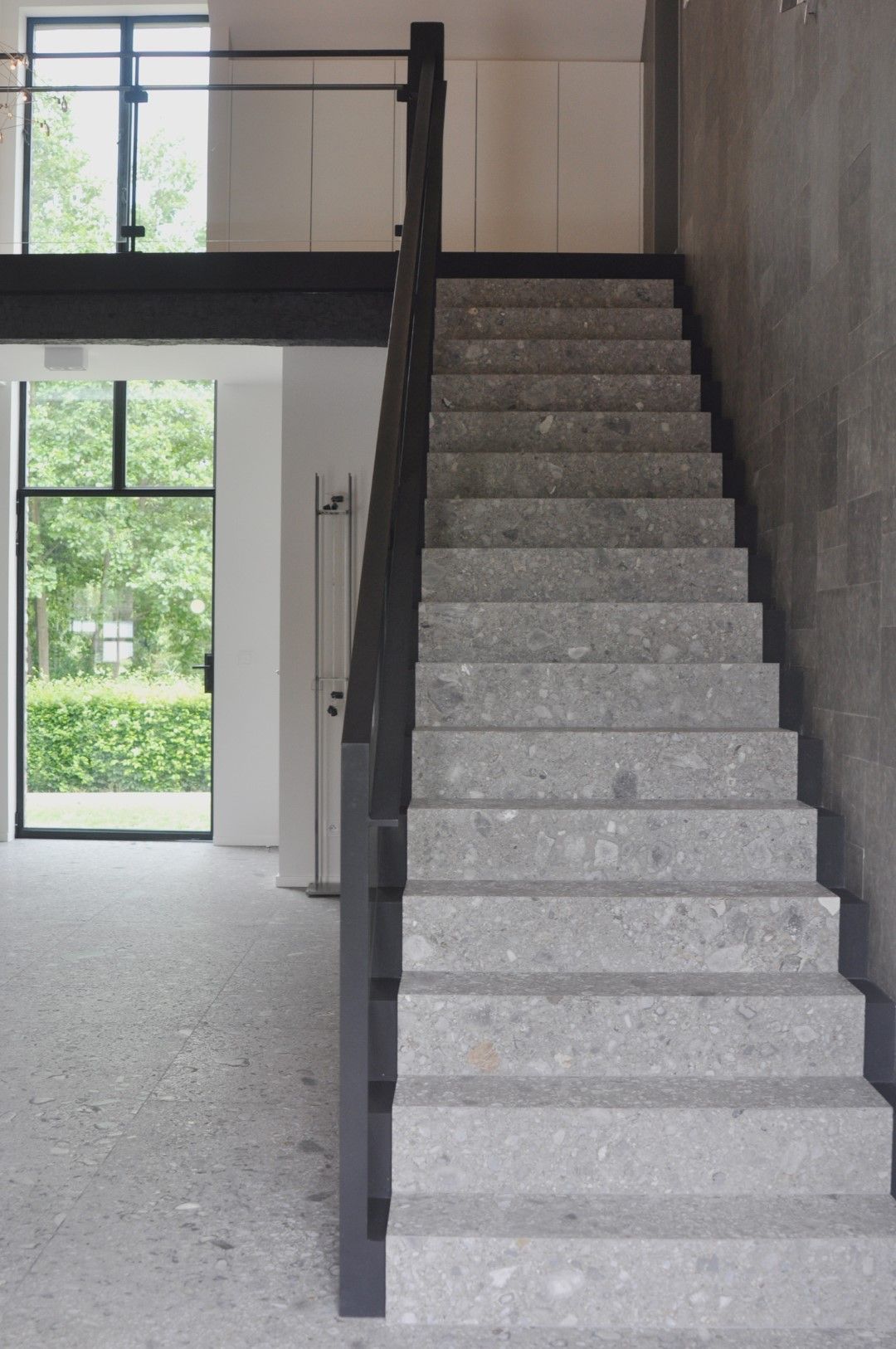 Stalen trap afgewerkt met natuursteen en met stalen trapleuning met glas